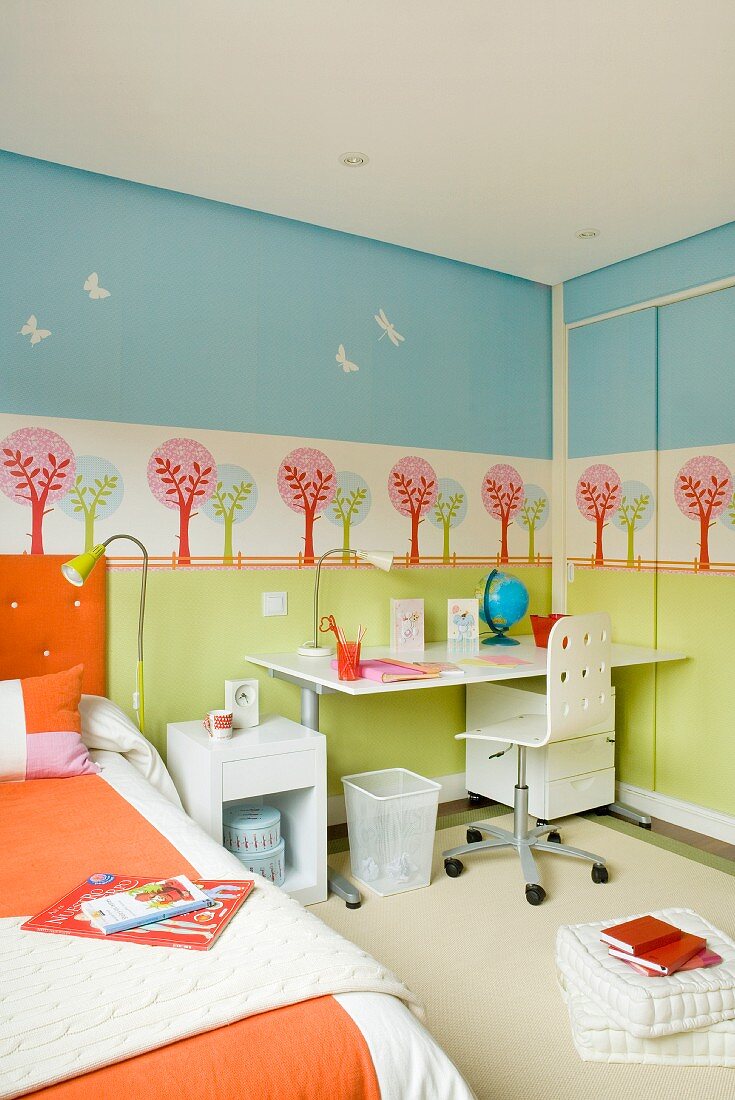 Pastel colors in a child's bedroom - stenciled wall behind a work station in neutral white and orange linens on the bed