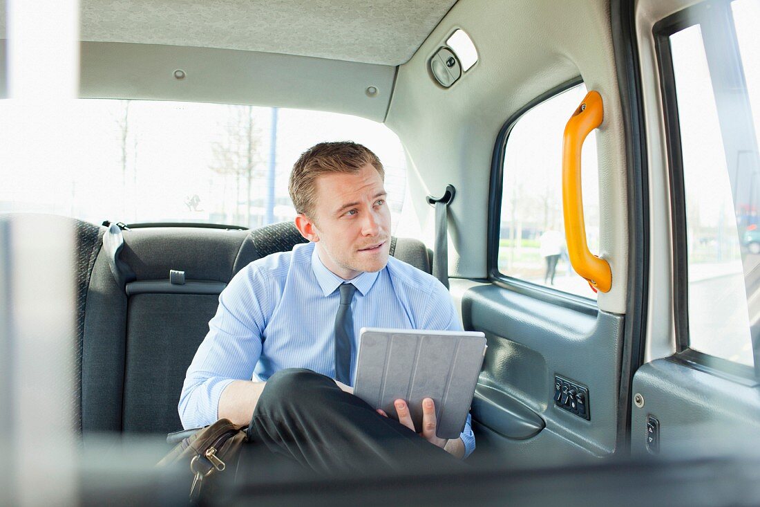 A business man with a tablet PC sitting in the back of a car