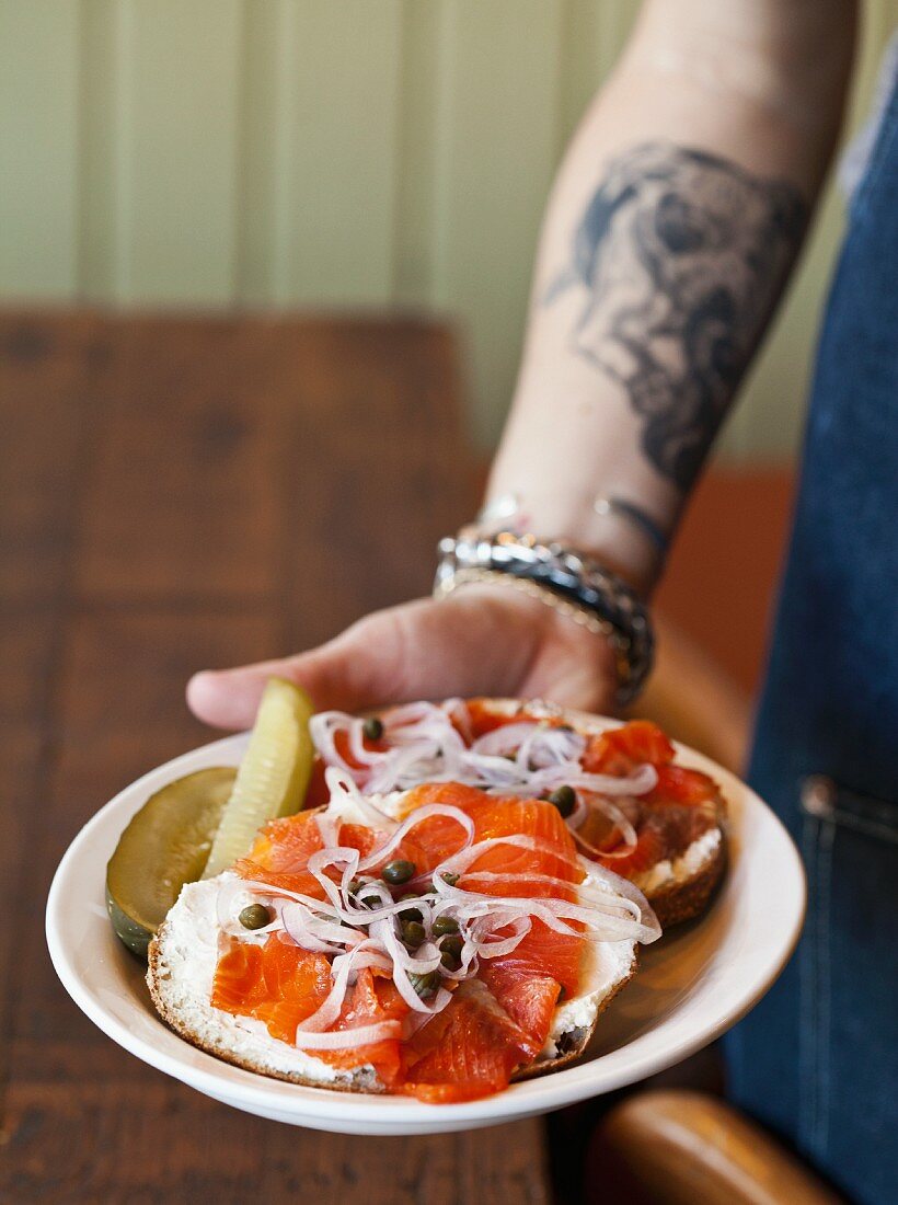 Hand serviert Bagel mit Lachs, Kapern und Zwiebeln