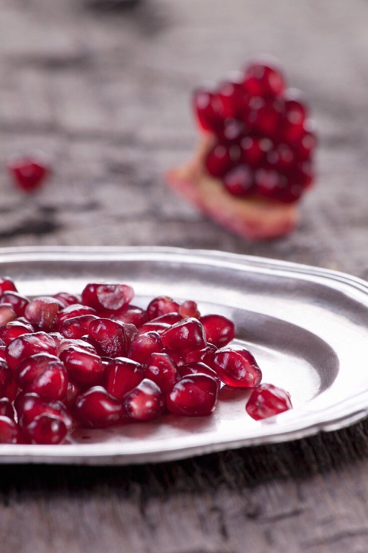 Pomegranate seeds on a silver plate and a piece of pomegranate