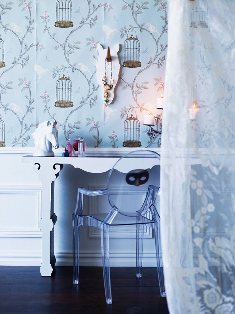 Designerstuhl aus Acrylglas und Porzellan Pferdekopf auf Schminktisch vor floral gemusterter Tapete; romantischer Voilevorhang im Vordergrund
