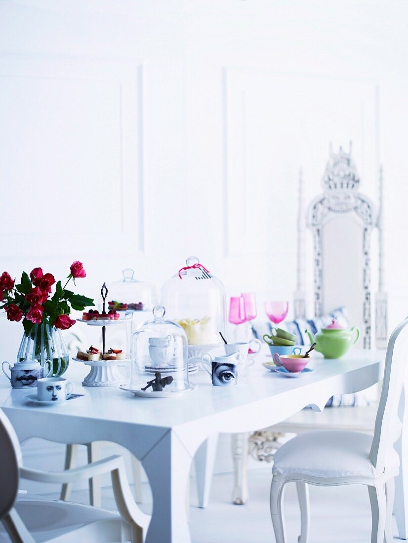 Antikisierende weiße Polsterstühle an romantisch weiss gedecktem Tisch mit pastellfarbenem Porzellan, Konfekt-Etagere und Glashauben