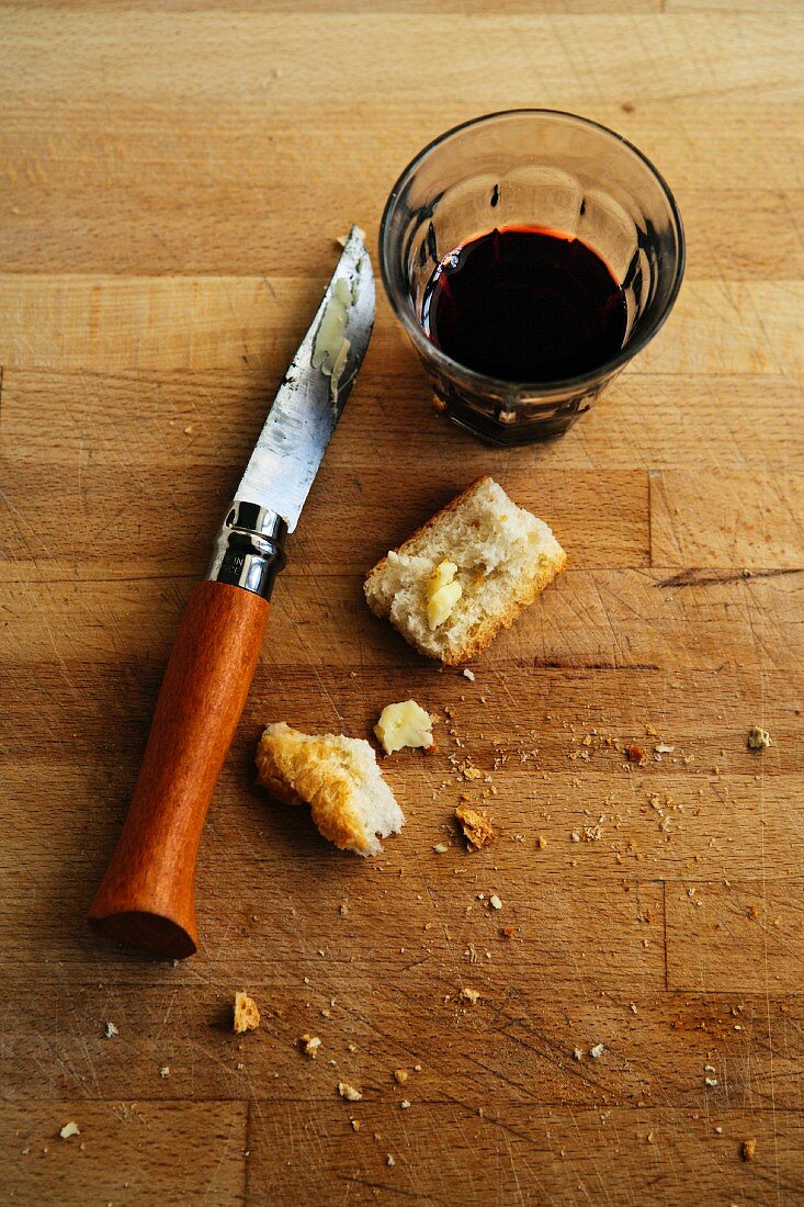 A glass of red wine, a knife and leftover bread on a wooden table
