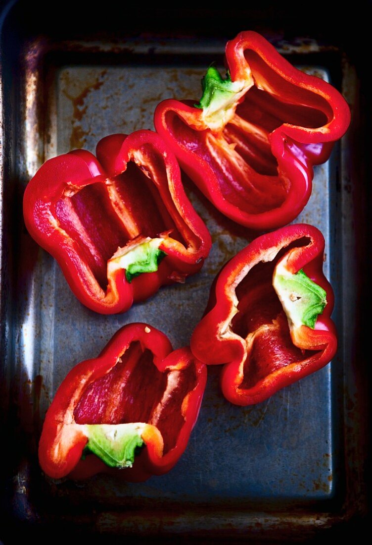 Halved red peppers on a baking tray (seen from above)