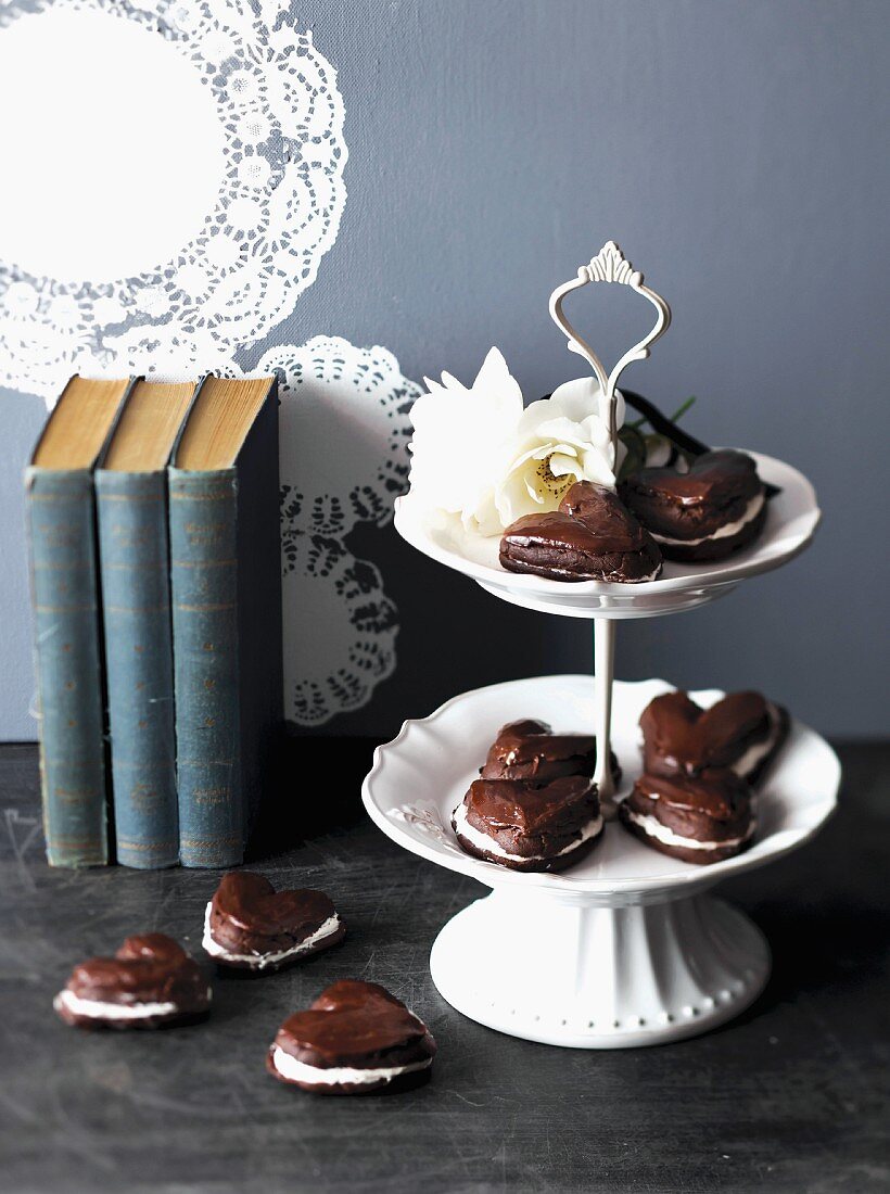 Chocolate hearts with cream filling, next to and on a tiered cake stand