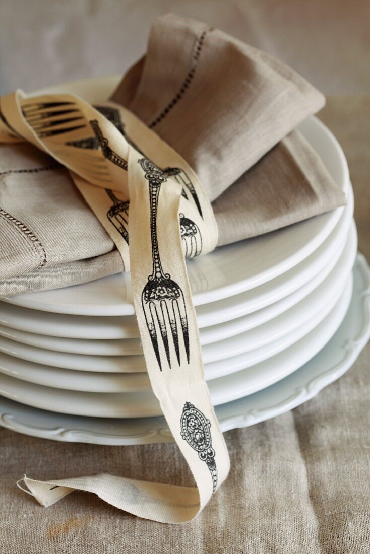 A napkin wrapped with a ribbon decorated with cutlery, on a stack of plates