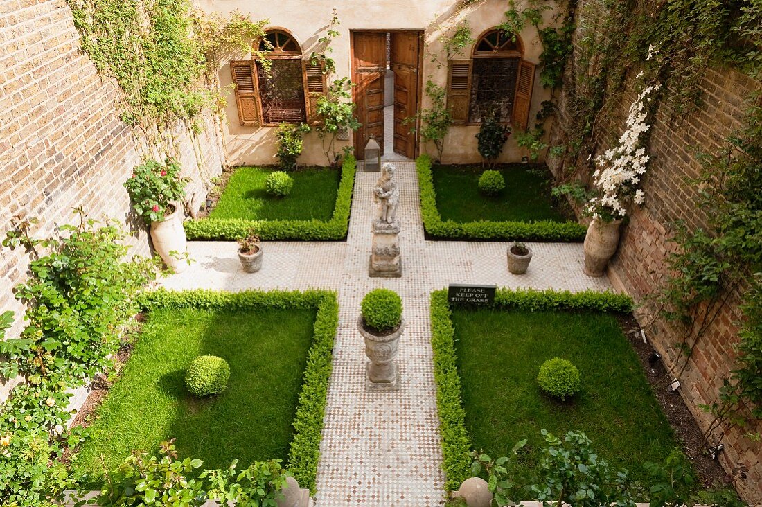 View of a symmetrically designed courtyard with a statue, boxwood hedge and paved walkway