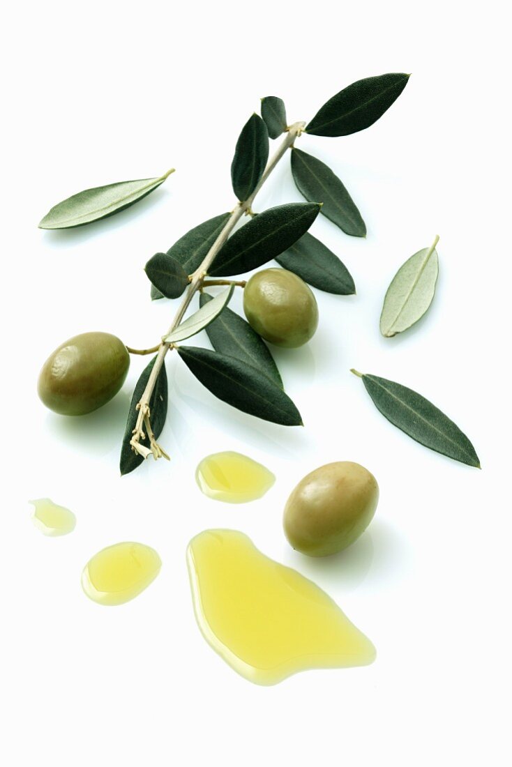 A olive sprig with olives next to a pool of olive oil