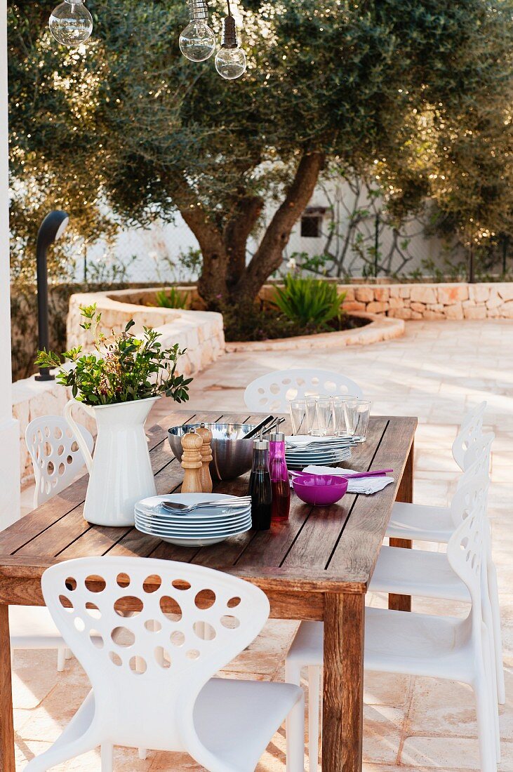 weiße Plastikstühle um hölzernen Esstisch auf einer Terrasse