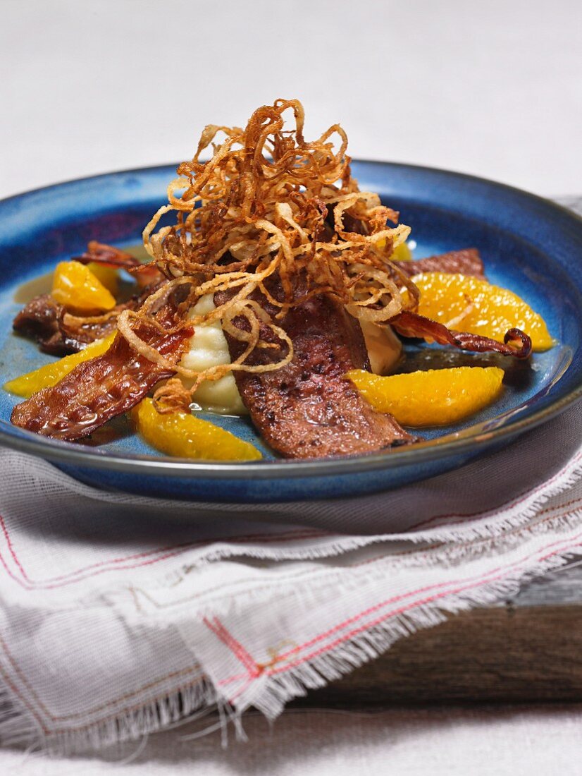 Liver with orange fillets and crispy onion rings on potato straw