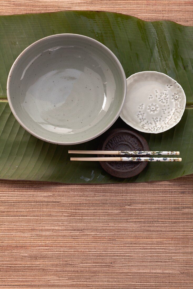 Bowls, plates and chopsticks on a banana leaf (Asia)