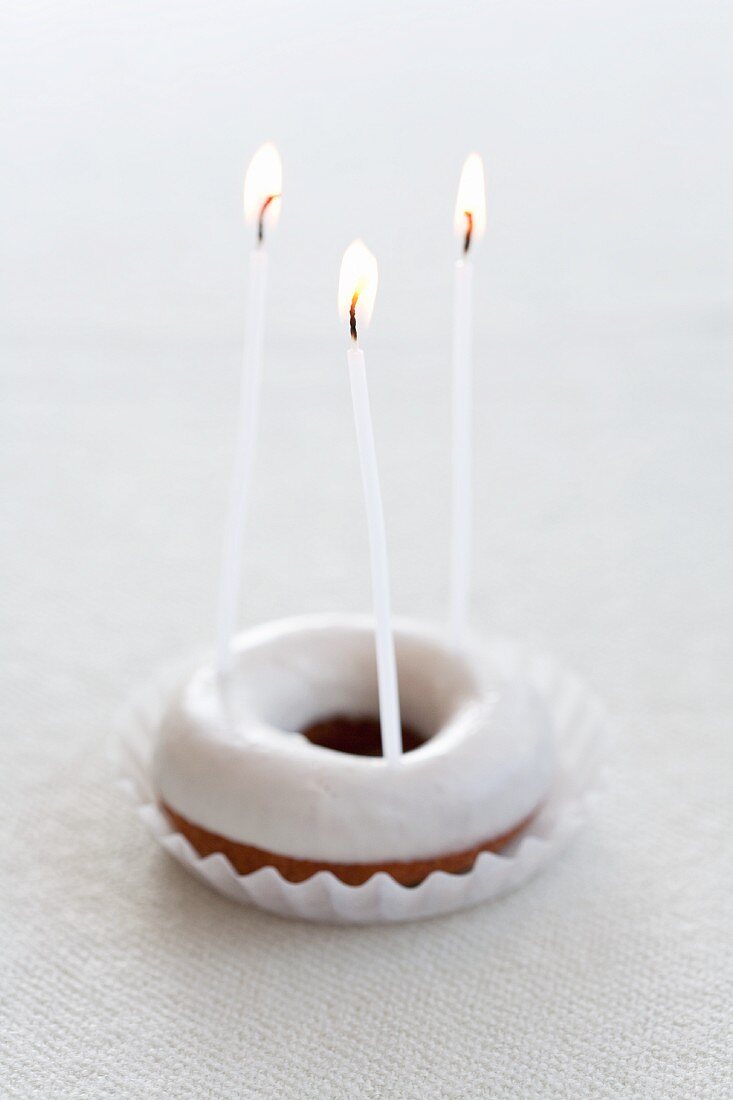 A doughnut with icing sugar and three candles