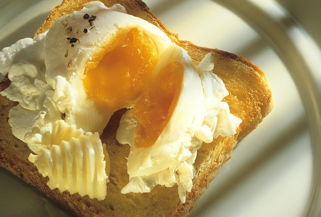 Pochiertes, halbiertes Ei mit Butterröllchen auf Toast