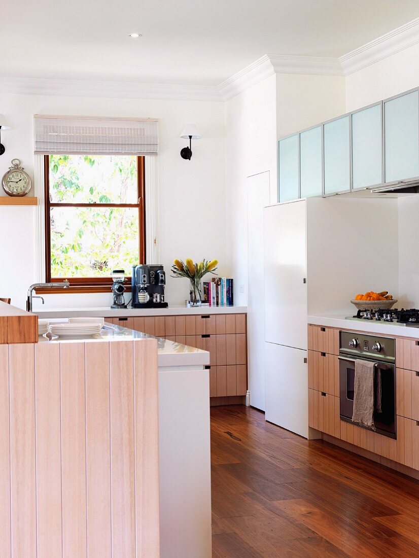 Fitted kitchen with pale, varnished wooden doors, frosted glass wall units and exotic-wood parquet floor