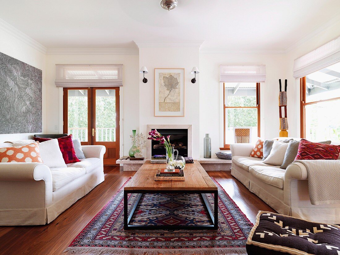 Pale sofas with scatter cushions and retro table on Oriental carpet in bright living room