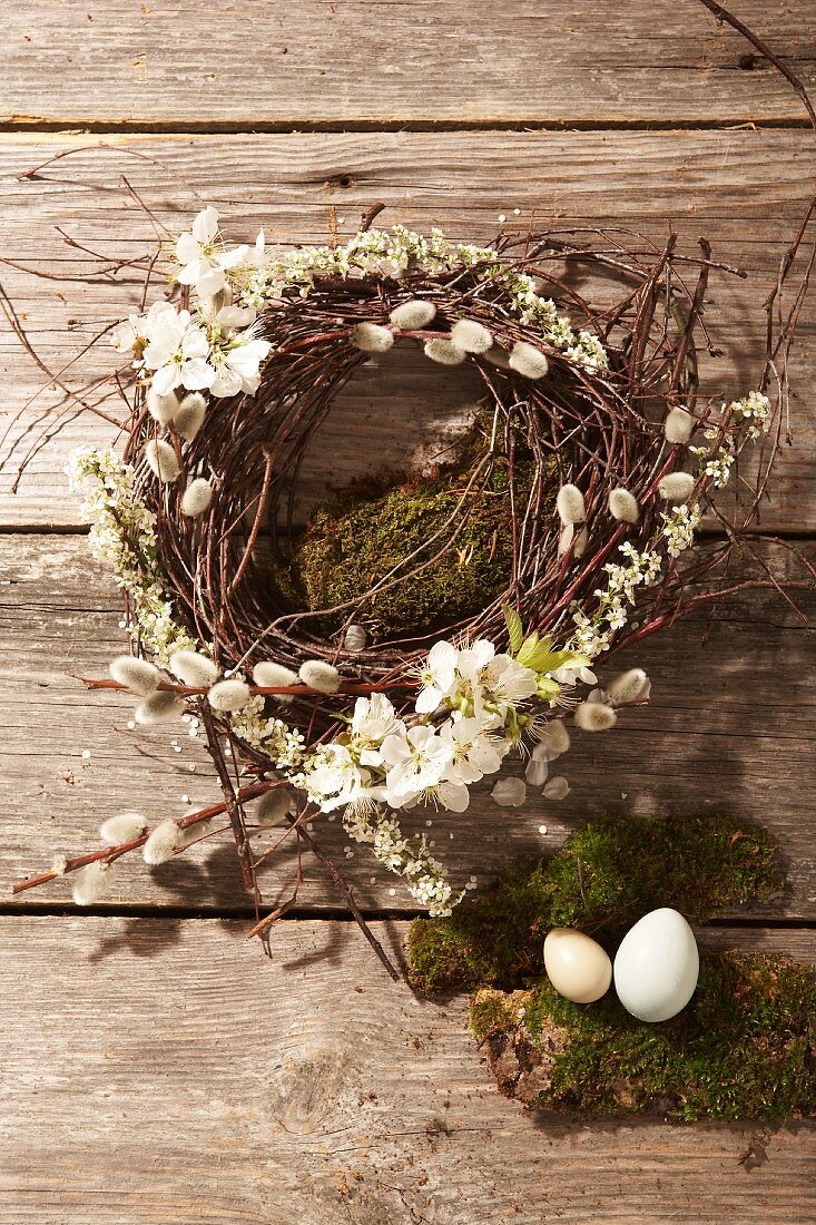Wreath made of pussy willow and fruit blossom, moss and Easter eggs on a wooden surface