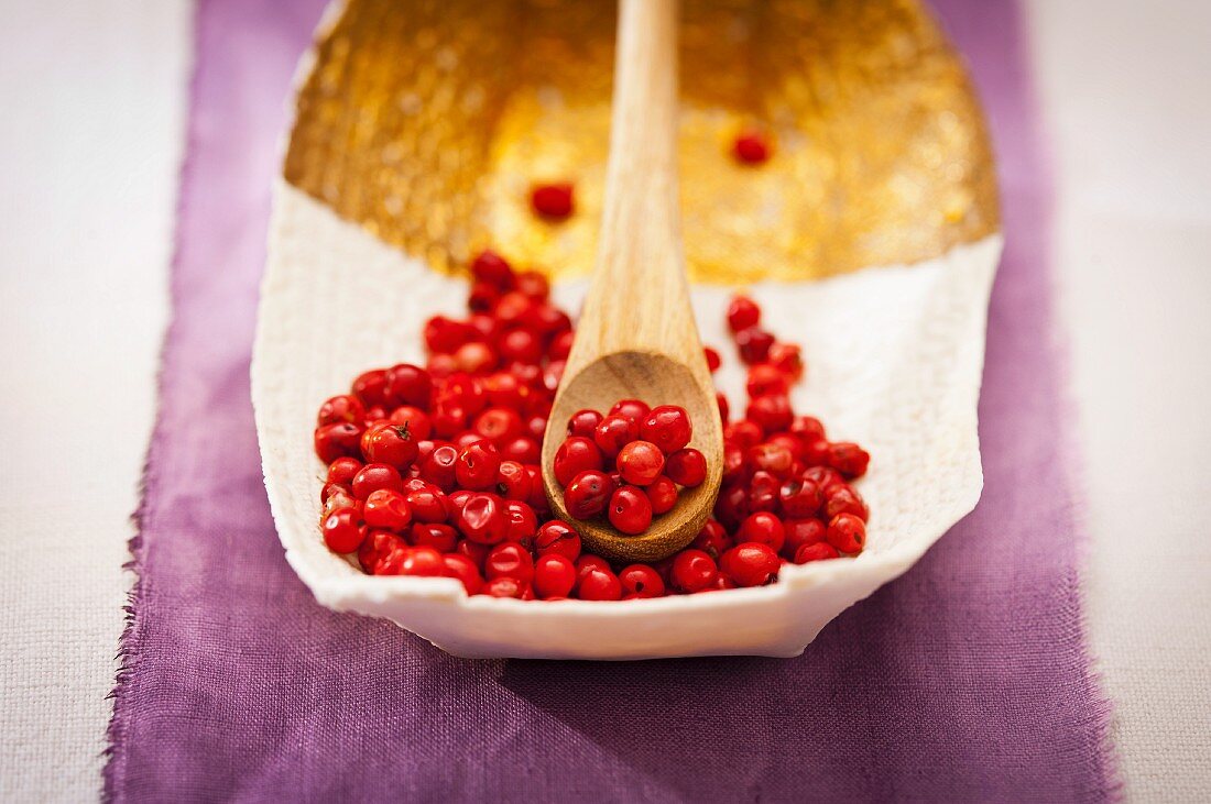 Pink peppercorns in a bowl and on a wooden spoon