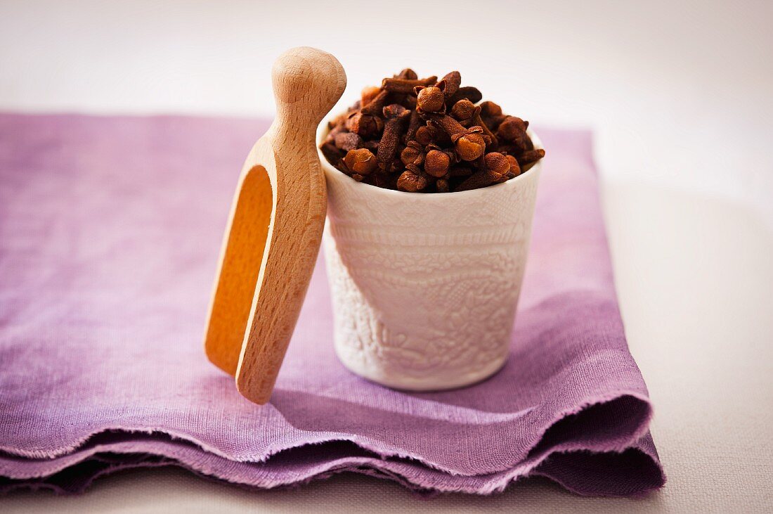 Cloves in a porcelain bowl with a wooden scoop