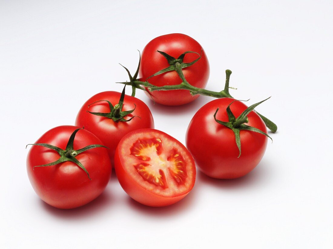 Four whole tomatoes and a halved tomato on a white surface