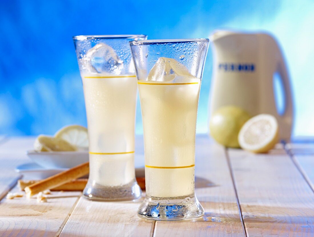 Two glasses of Pernod with ice cubes, lemons and breadsticks