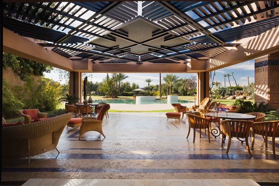 A painted wood screen provides shade over a garden terrace with tiled flooring and wicker furniture