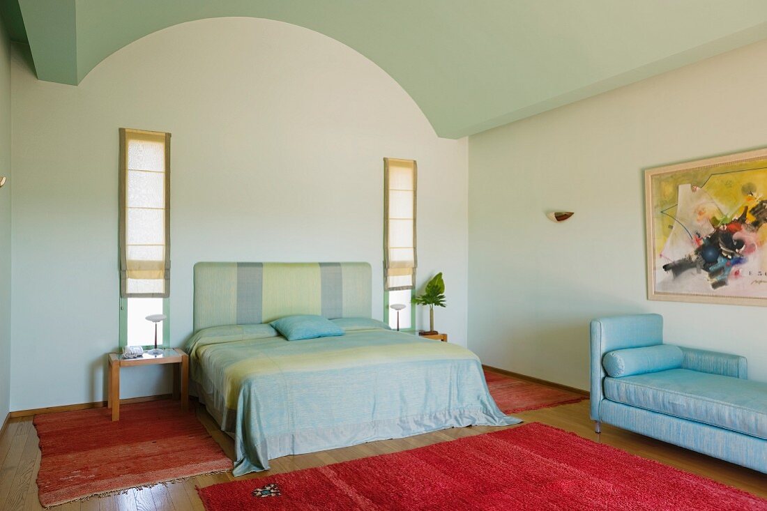 Simple bedroom with red handmade rugs and pale fabrics on the bed and daybed