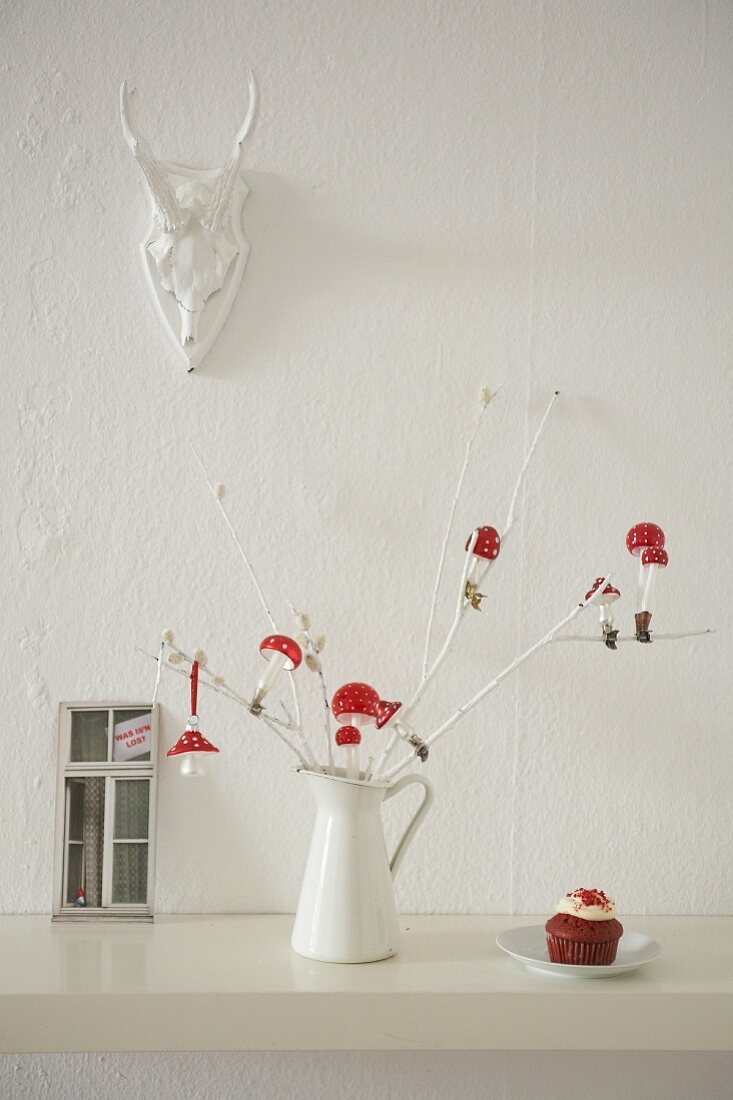 A twig decorated with toadstools and cupcakes against a wall hung with a hunting trophy