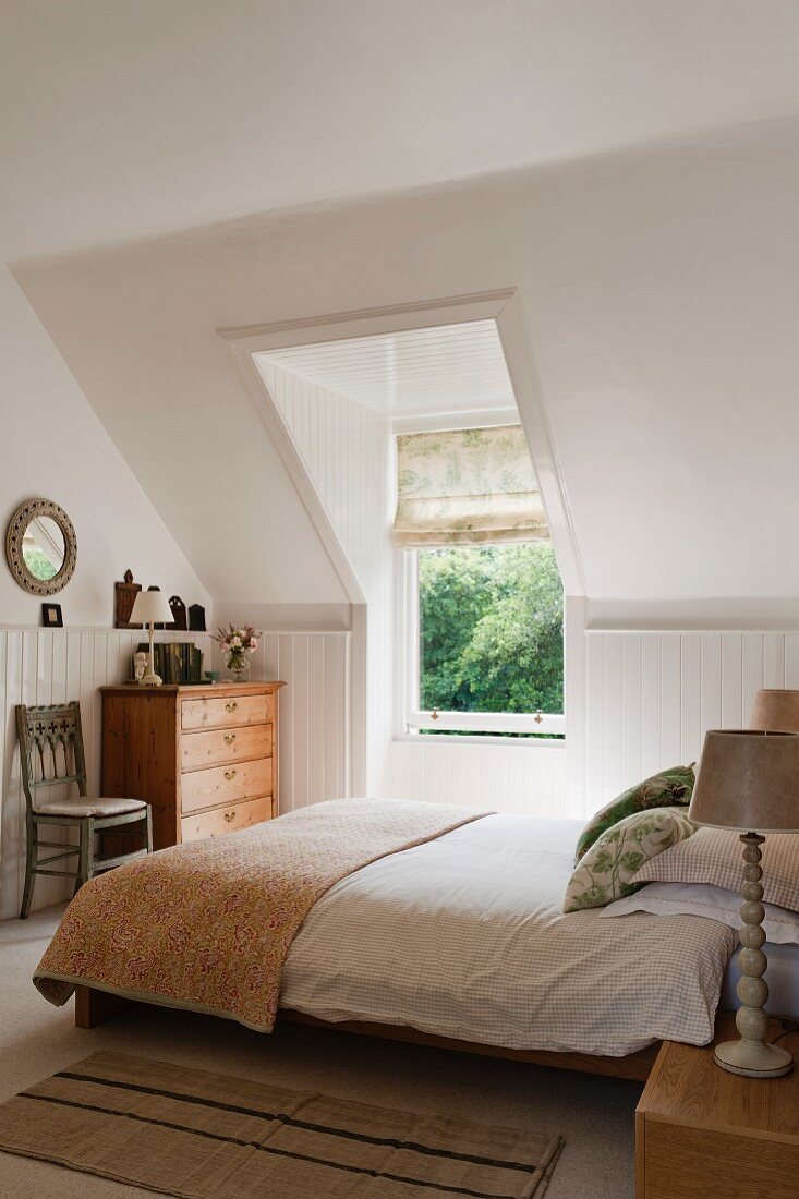Helles Schlafzimmer mit großem Fenster unter der Dachschräge; auf dem Bett ein Quilt-Überwurf