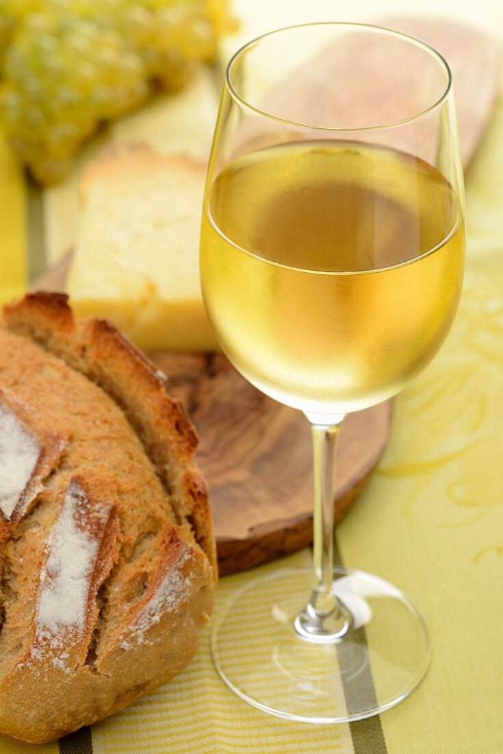A glass of white wine, bread, cheese and grapes