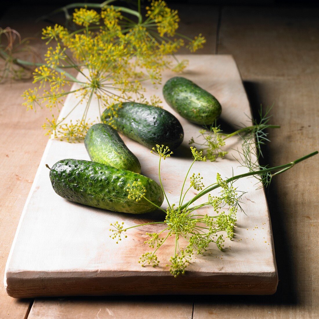 Gherkins and dill flowers on a wooden board