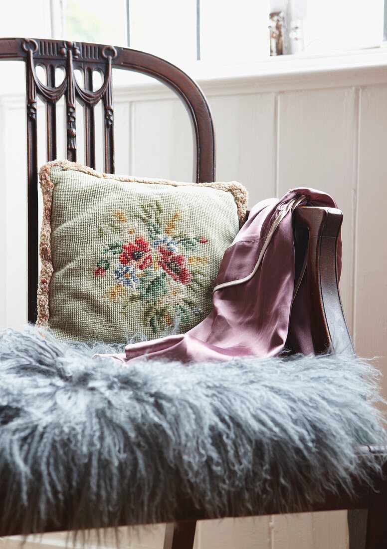 Floral embroidered cushion and grey fur mat on antique, English-style wooden chair