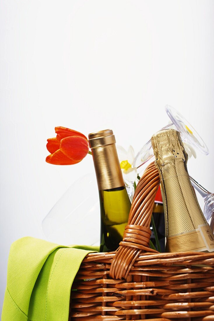 A bottle of champagne and a bottle of wine in a picnic basket with glasses