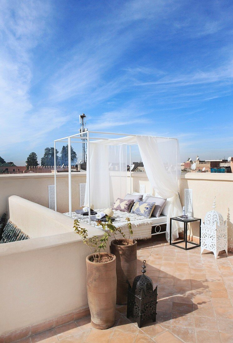 Blauer Himmel über orientalischer Dachterrasse mit Pflanzentöpfen und modernem Himmel-Tagesbett auf Terracottafliesenboden