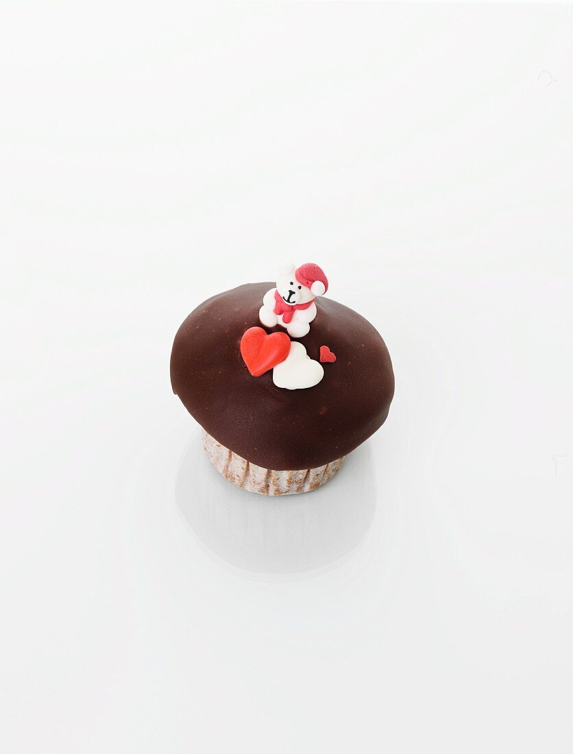 A cupcake decorated with a teddy bear and hearts