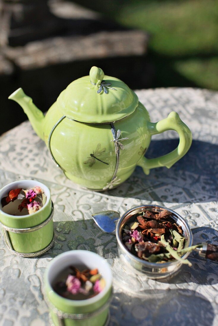 A lime-green teapot with silver dragonfly motif and matching tea tumblers on an antique garden table