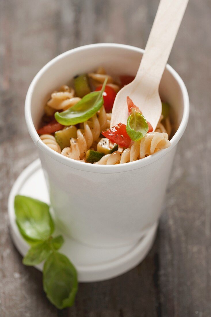 Fusilli mit Tomaten, Zucchini und Basilikum in einem Pappbecher