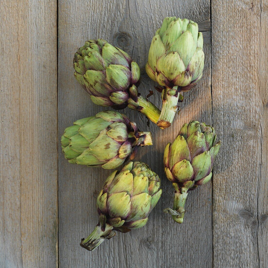 Five artichokes on a wooden surface