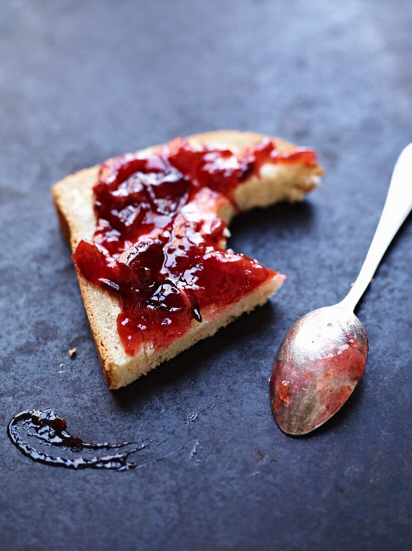 A slice of bread topped with damson jam with a bite taken out