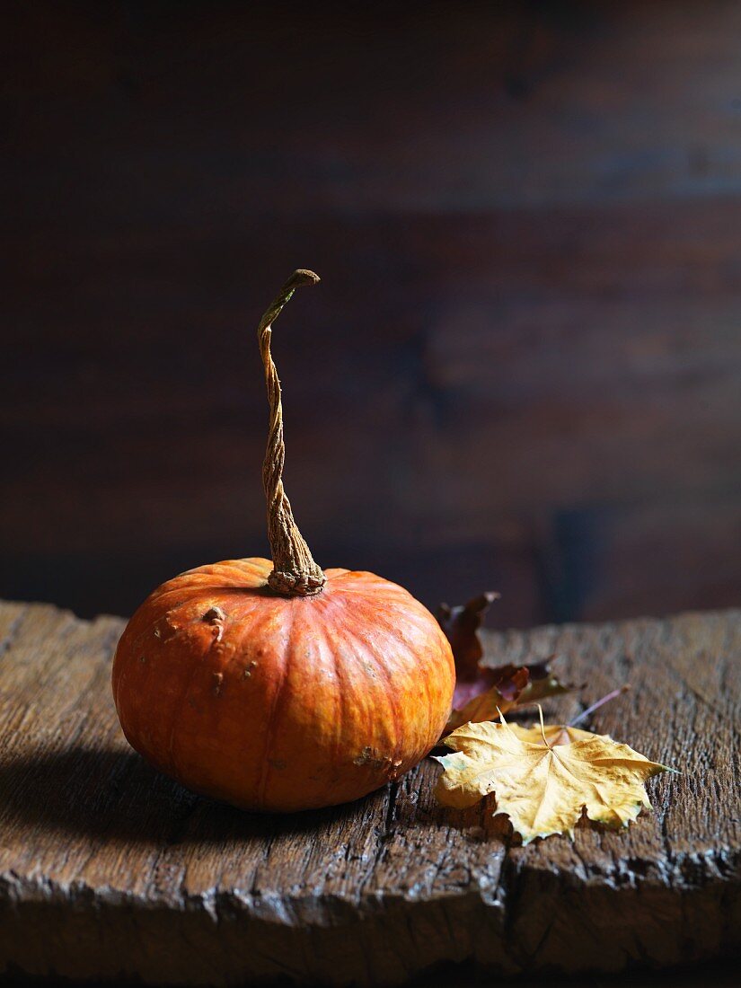 An orange pumpkin with autumnal leaves on a wooden board