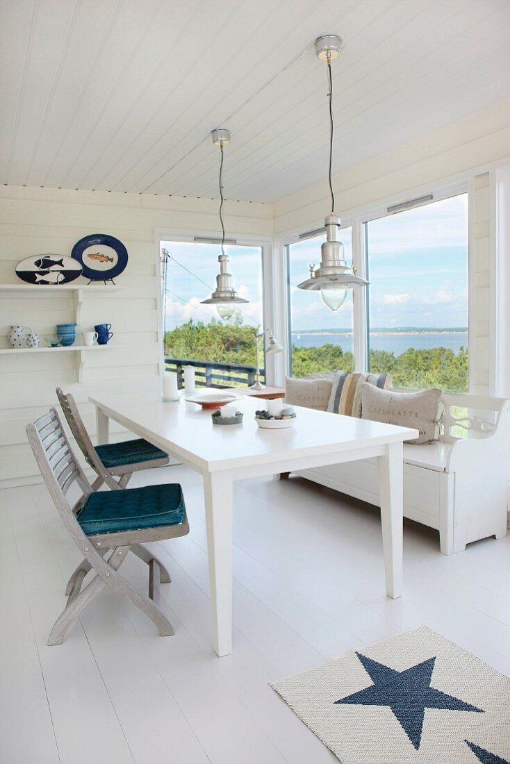 White dining table and folding wooden chairs by a window with a view