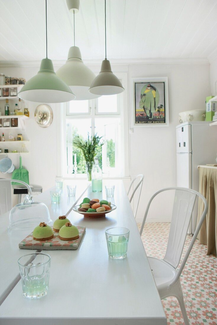 Pendant lamps in various shades of green above freshly baked cakes on white dining table