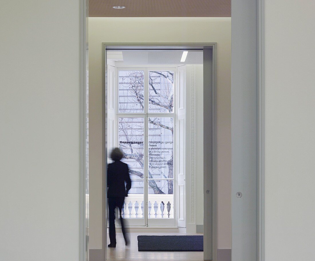 Blick durch offene Tür und Gang auf Frau vor Balkontür stehend (Goethe Institut, London)