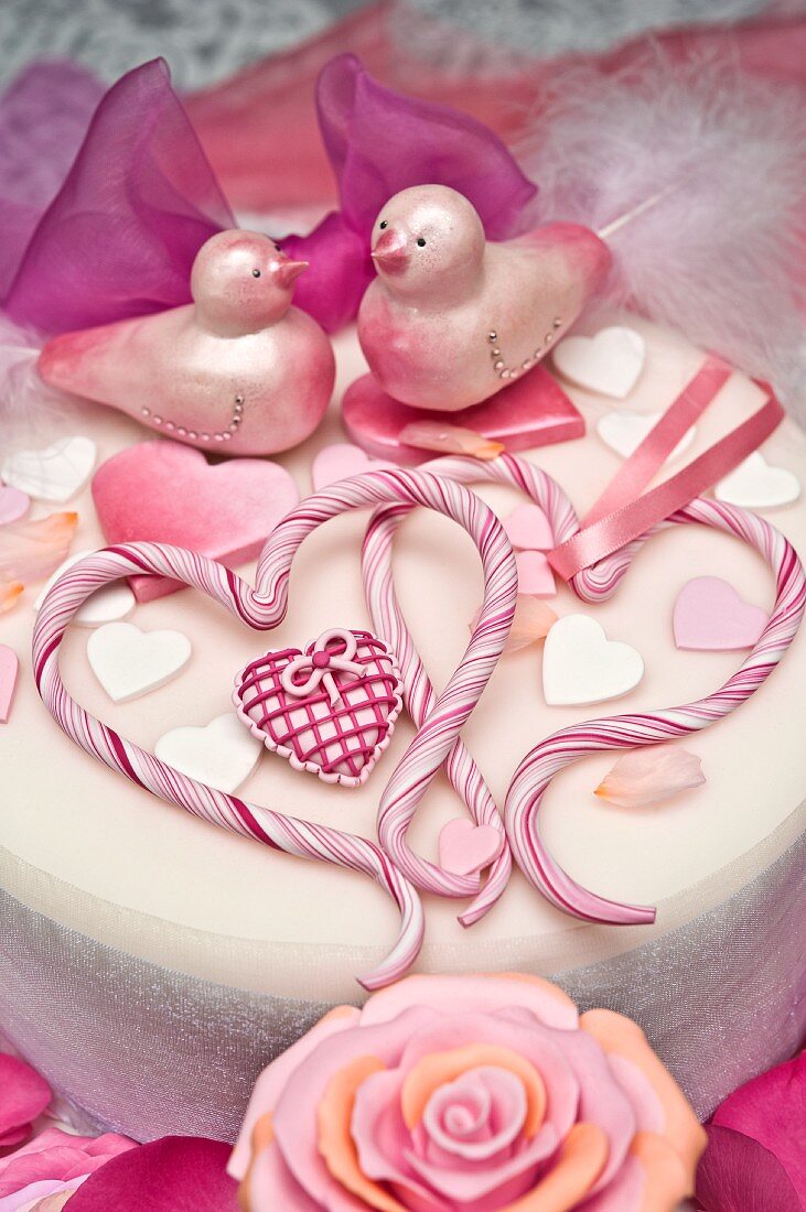 weiße Torte mit Herzen, Vögeln, Rosenblüten und Schleife dekoriert