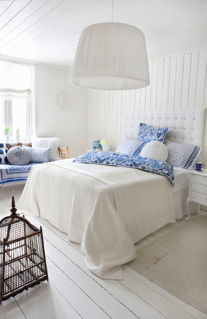 Bright, pale bedroom in white with blue accents and antique birdcage