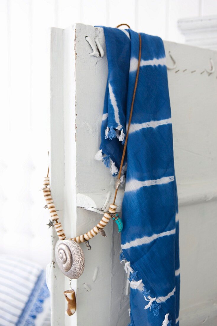 Vintage Schranktür, mit gebatiktem Tuch in Blau und Weiß und einer darüberhängenden Kette mit Muschelanhänger