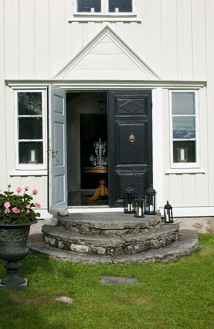 Entrance of traditional Swedish wooden house with round steps leading to black front door