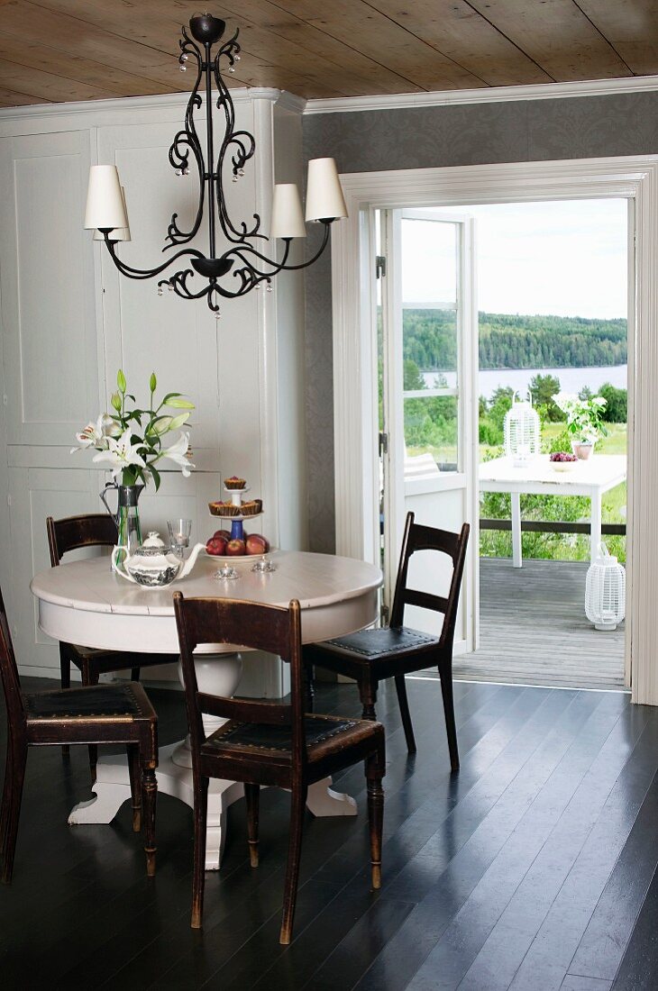 Comfortable dining room with pastel pink table and antique chairs and view of open landscape with lake through terrace doors