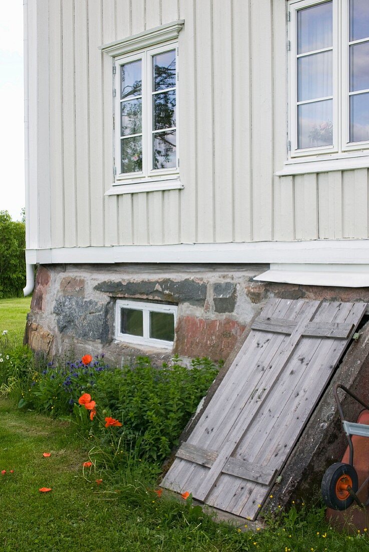 Facade of pale wooden house with weathered board door leading to cellar