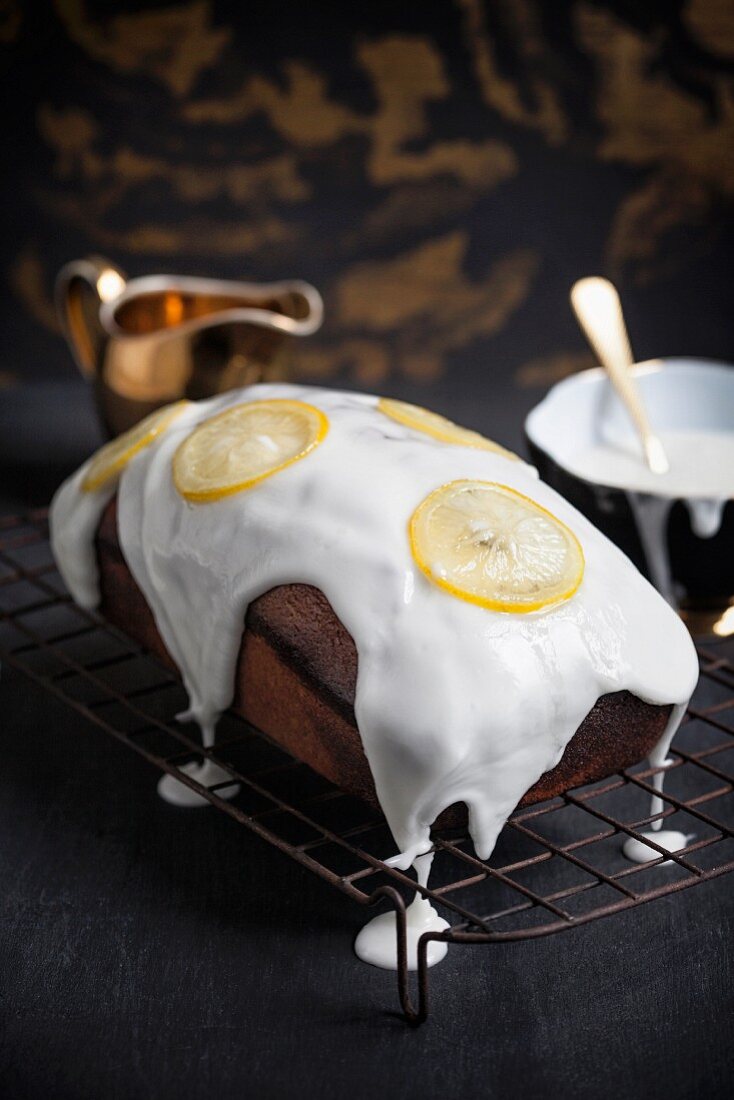 An iced lemon cake decorated with lemon slices on a wire rack