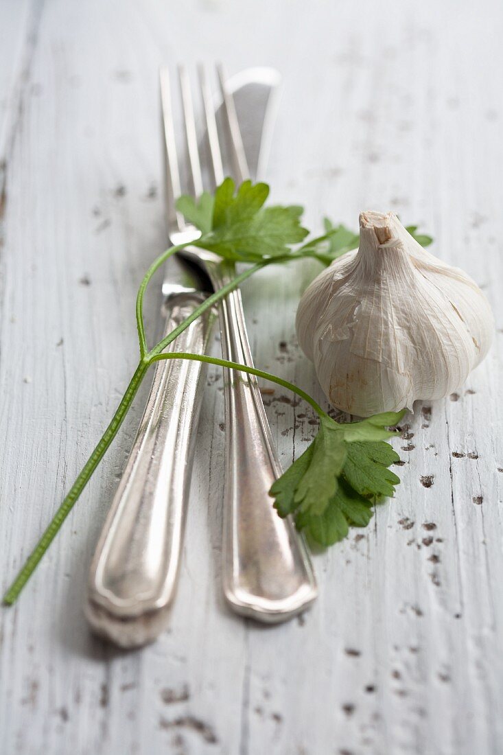 Silver cutlery, flat-leaf parsley and a bulb of garlic